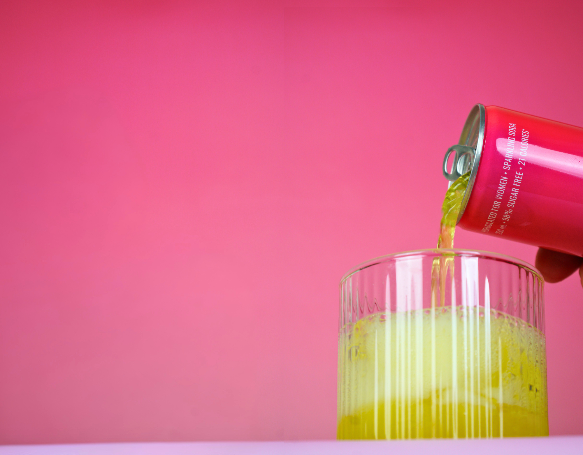Pink JUNA sparkling soda being poured from a can into a glass against a bright pink background, showing the fizzy functional beverage formulated for women